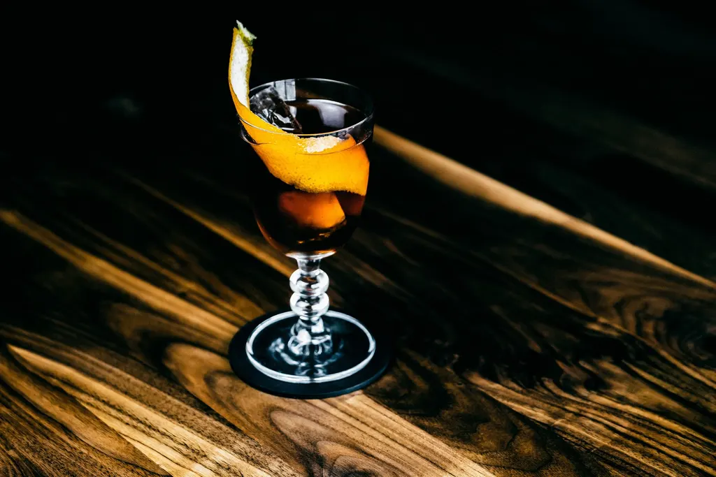 Craft cocktail with an orange twist on a wooden bar