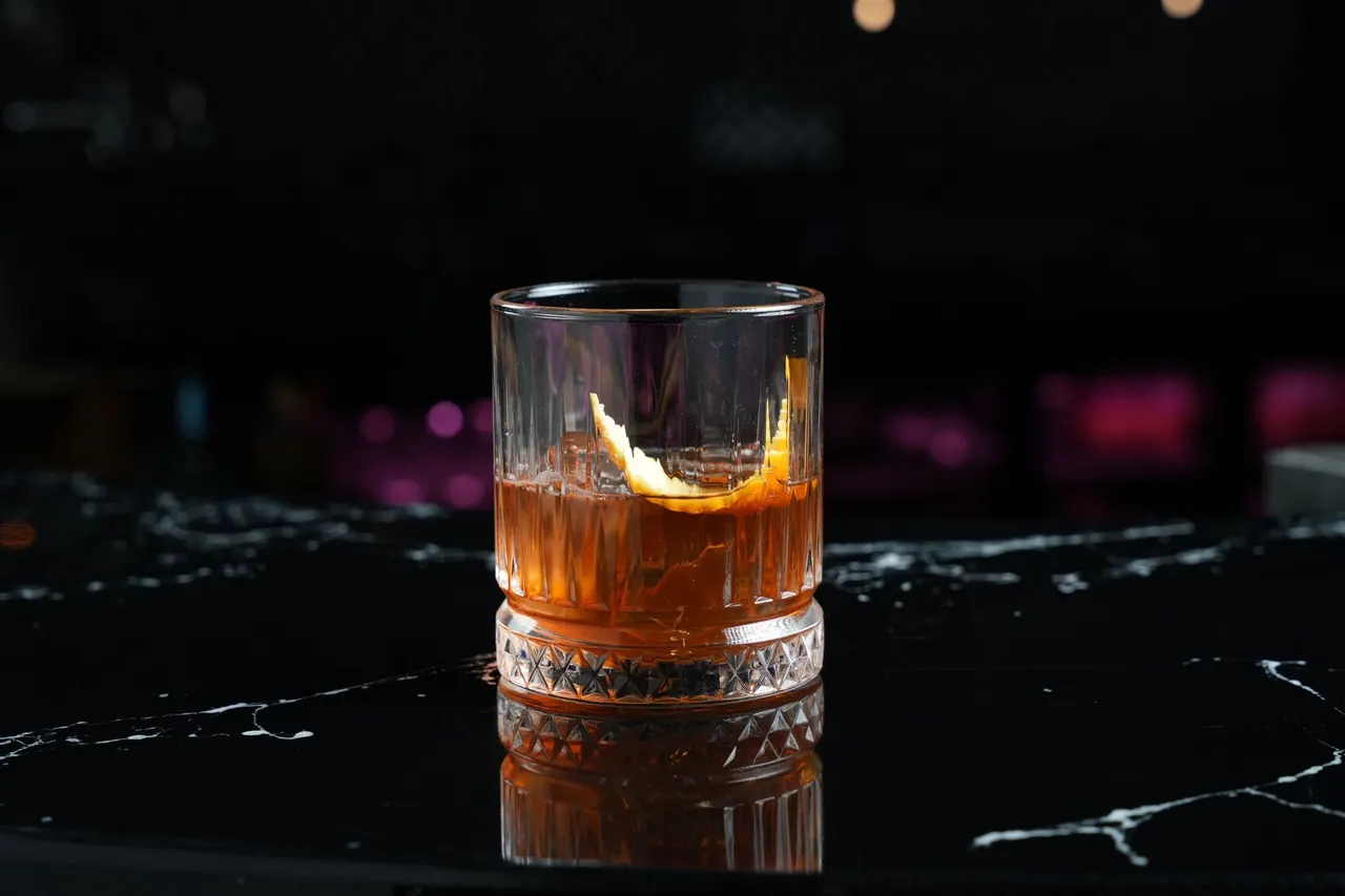 An old fashioned cocktail with an orange twist on a dark bar
