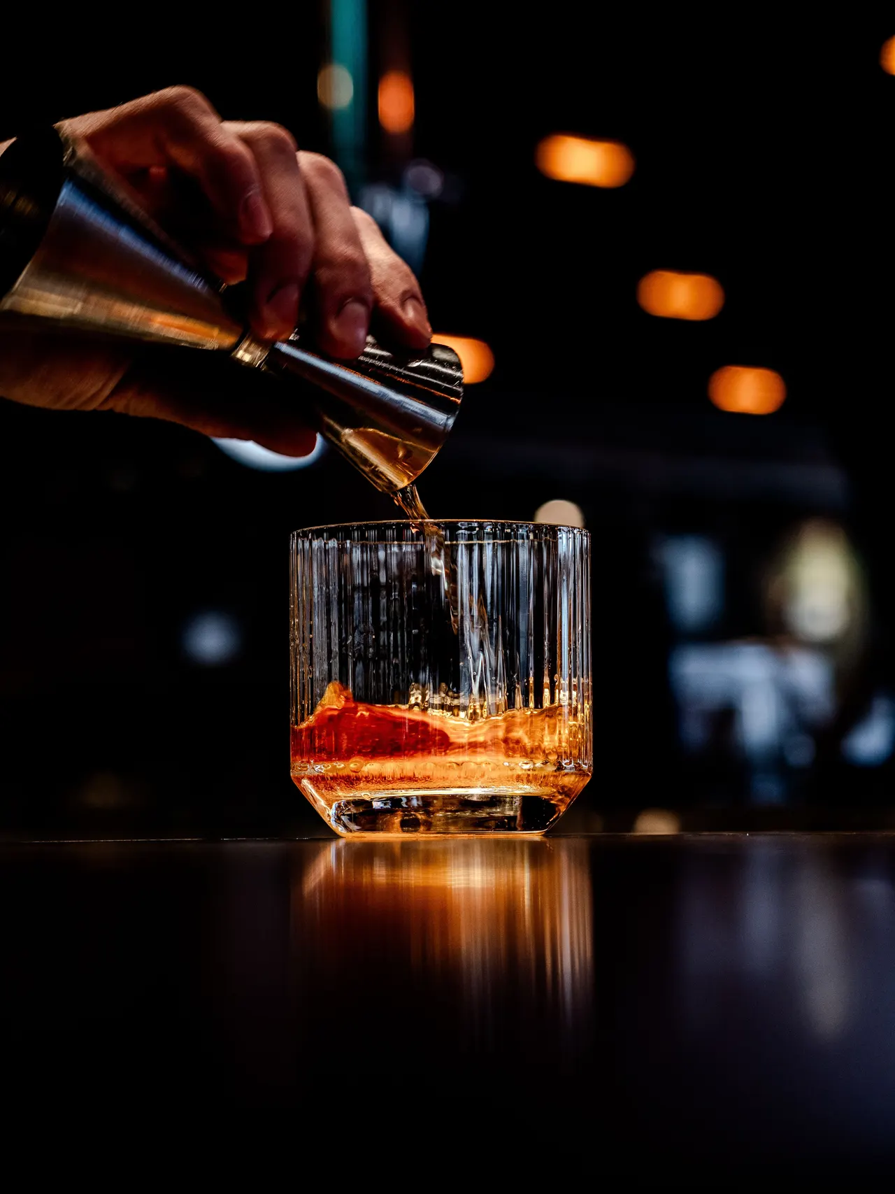 A bartender pouring whiskey into a ribbed glass at a dark bar
